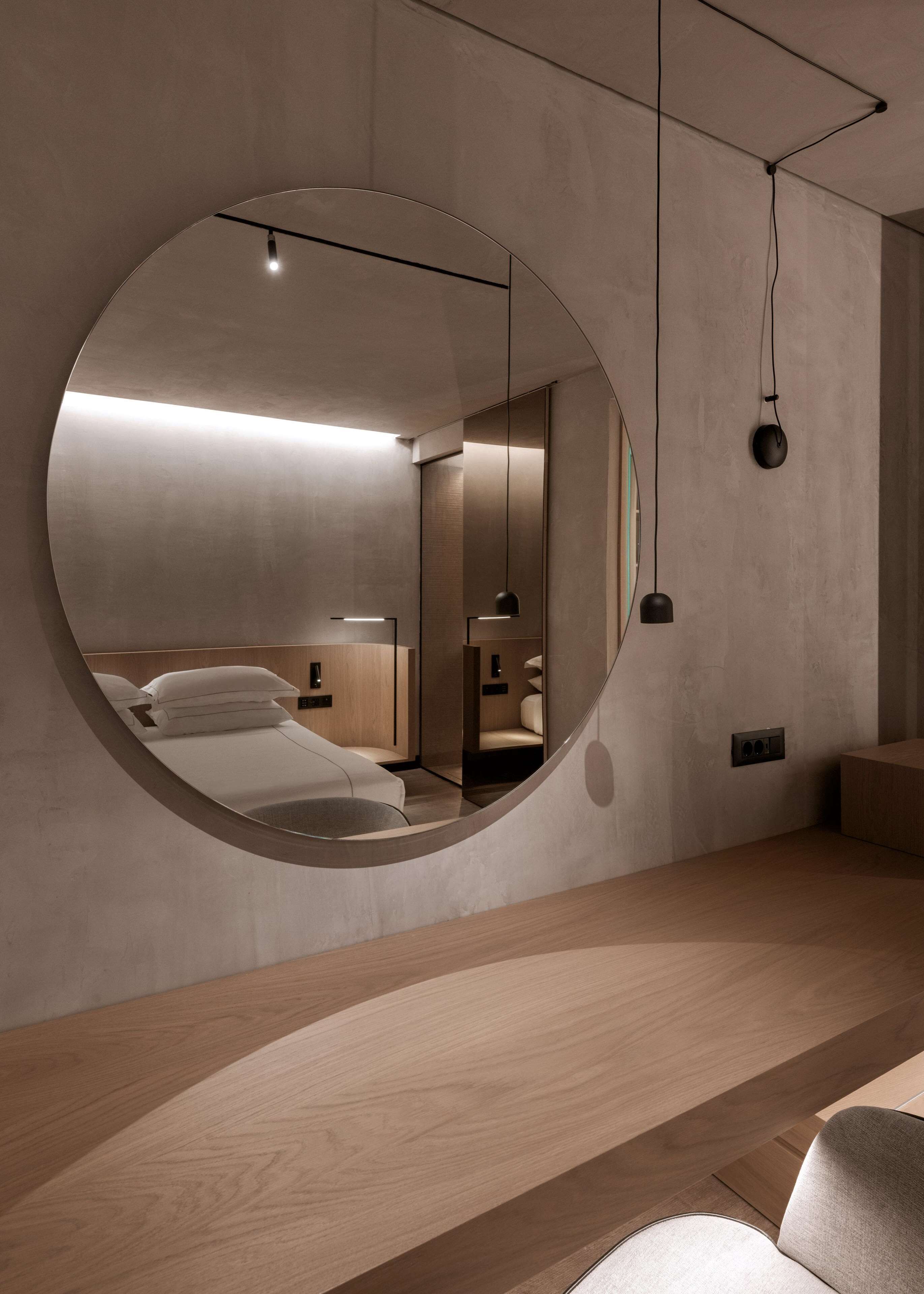 A modern bedroom with a large round mirror, a wooden bed frame, and a bedside table.
