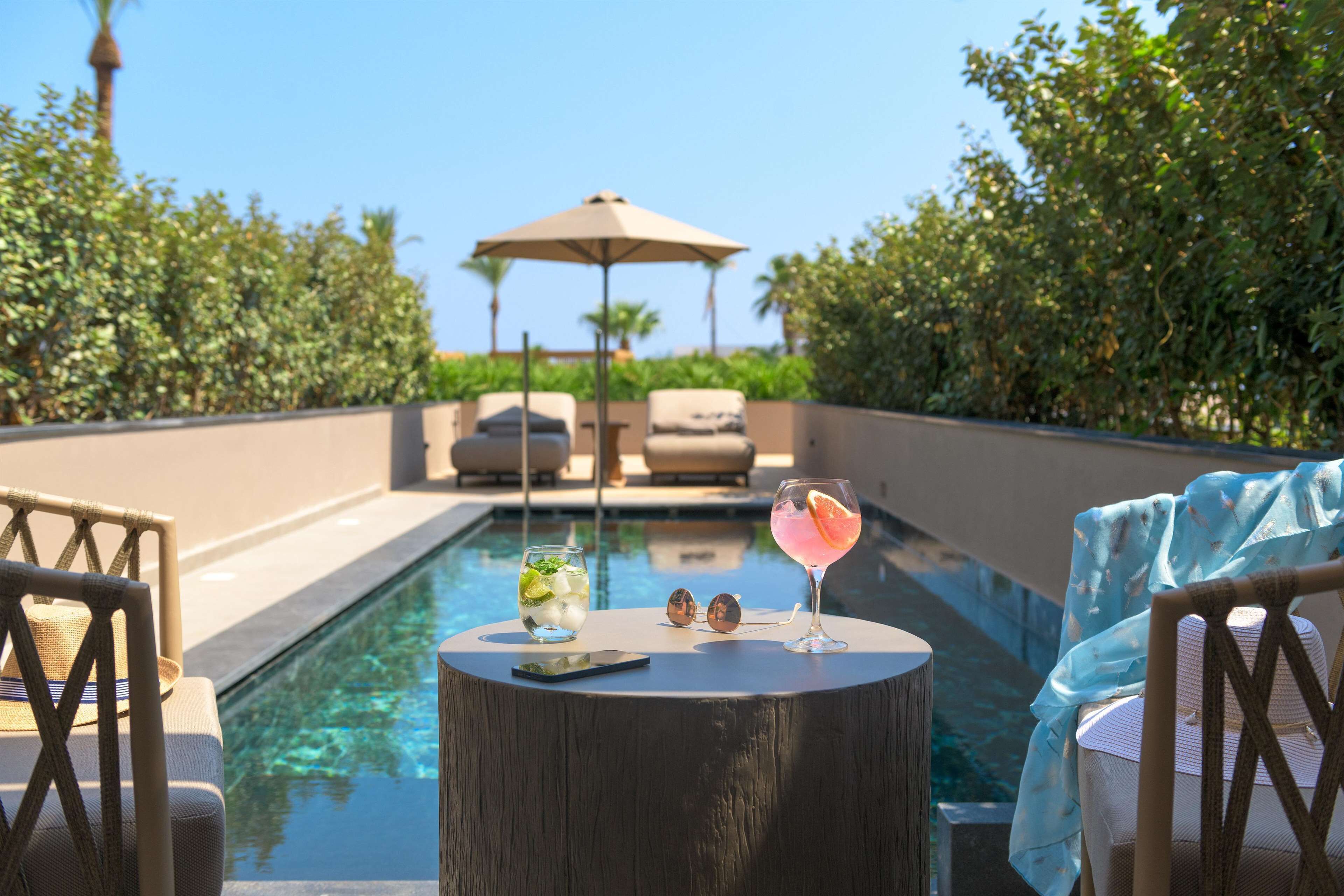 A poolside area with lounge chairs, a table with a drink, and a gazebo in the background.