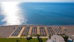 An aerial view of a beachside hotel with rows of sun loungers and umbrellas, a sandy beach, and the ocean in the background. - Ammades All Suites Beach Hotel & Spa - Adults Only (Rhodes)