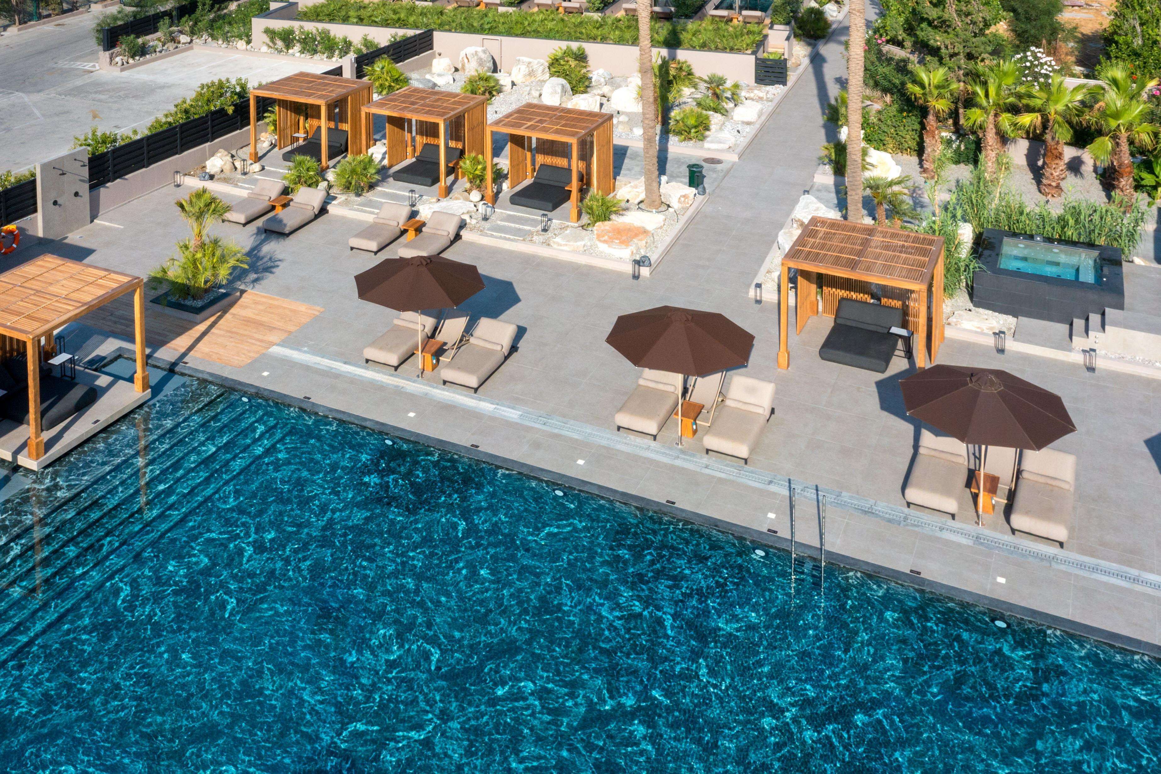 Ein Poolbereich im Freien mit Liegestühlen und Sonnenschirmen, umgeben von viel Grün und einem kühlen, blauen Pool.