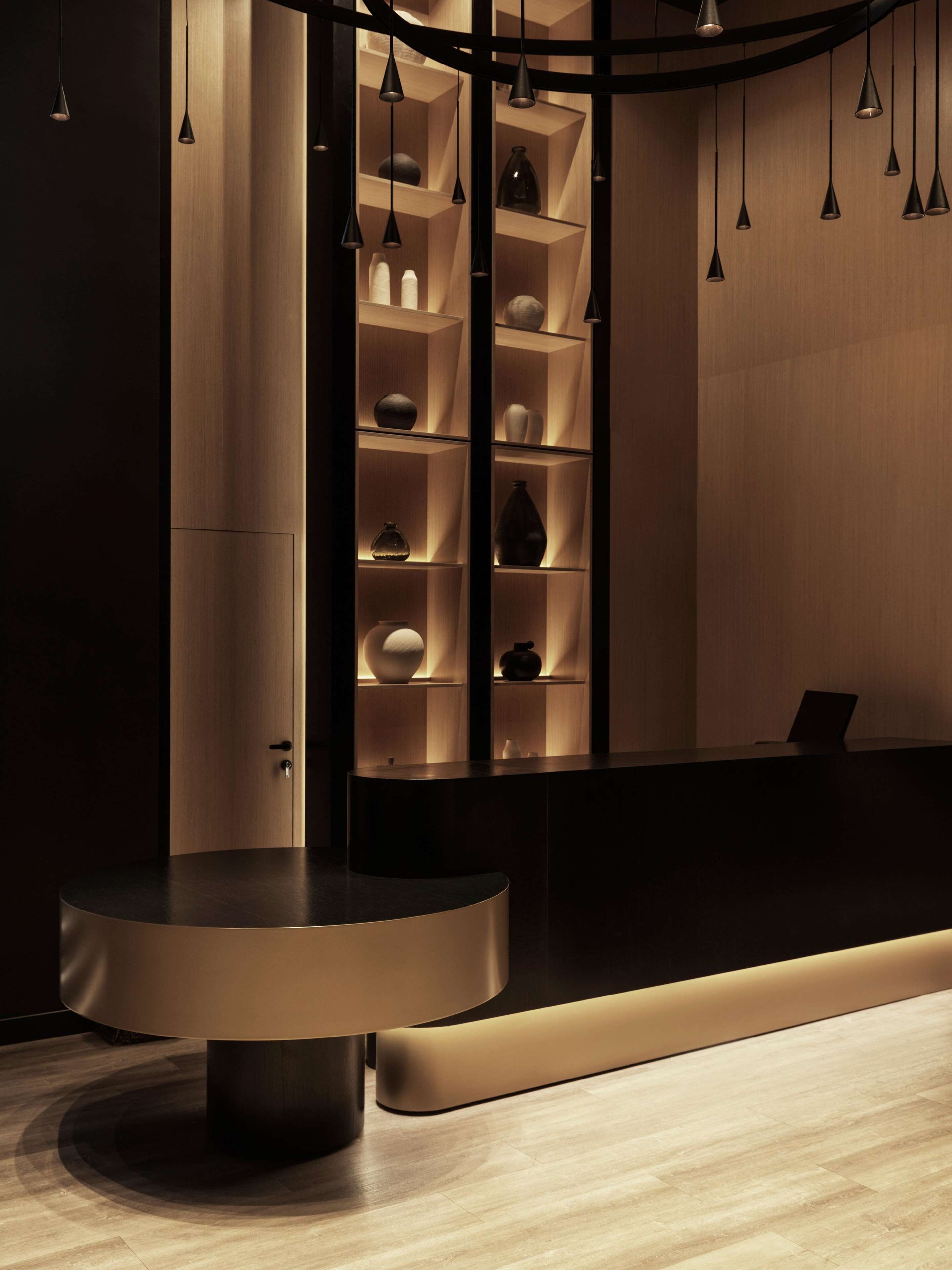 Un área de recepción moderna con un mostrador curvo, estanterías de madera con adornos e iluminación colgante.