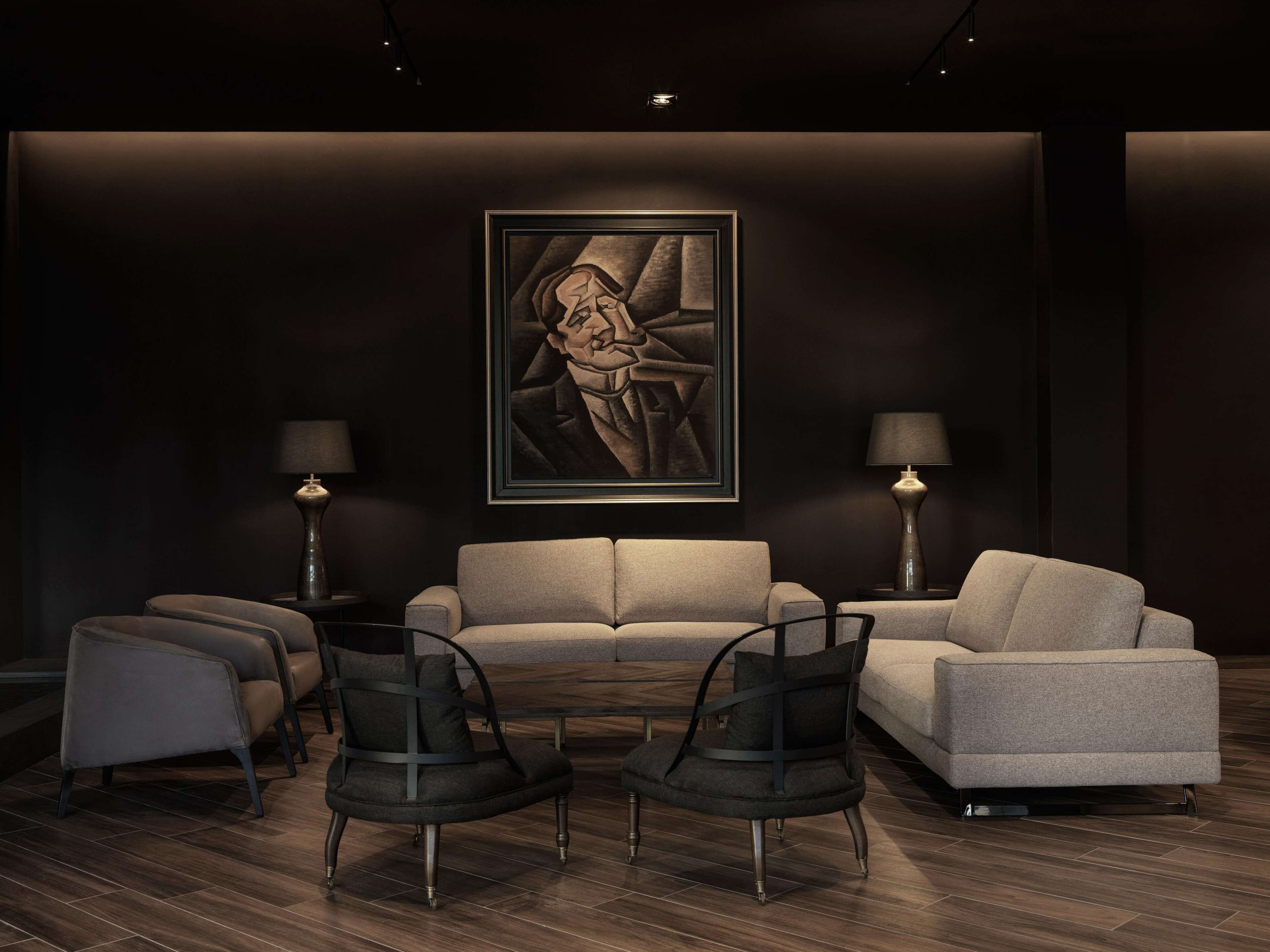 Un salón moderno con una paleta de colores oscuros, que incluye un sofá, dos sillones, una mesa de centro y dos lámparas de pie.