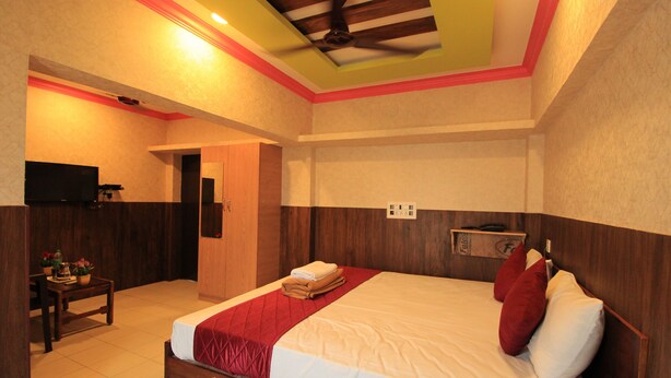 A bedroom with a bed, a wooden headboard, a bedside table with a lamp, and a television on the wall. - M.G.R. Park Inn (Viluppuram)