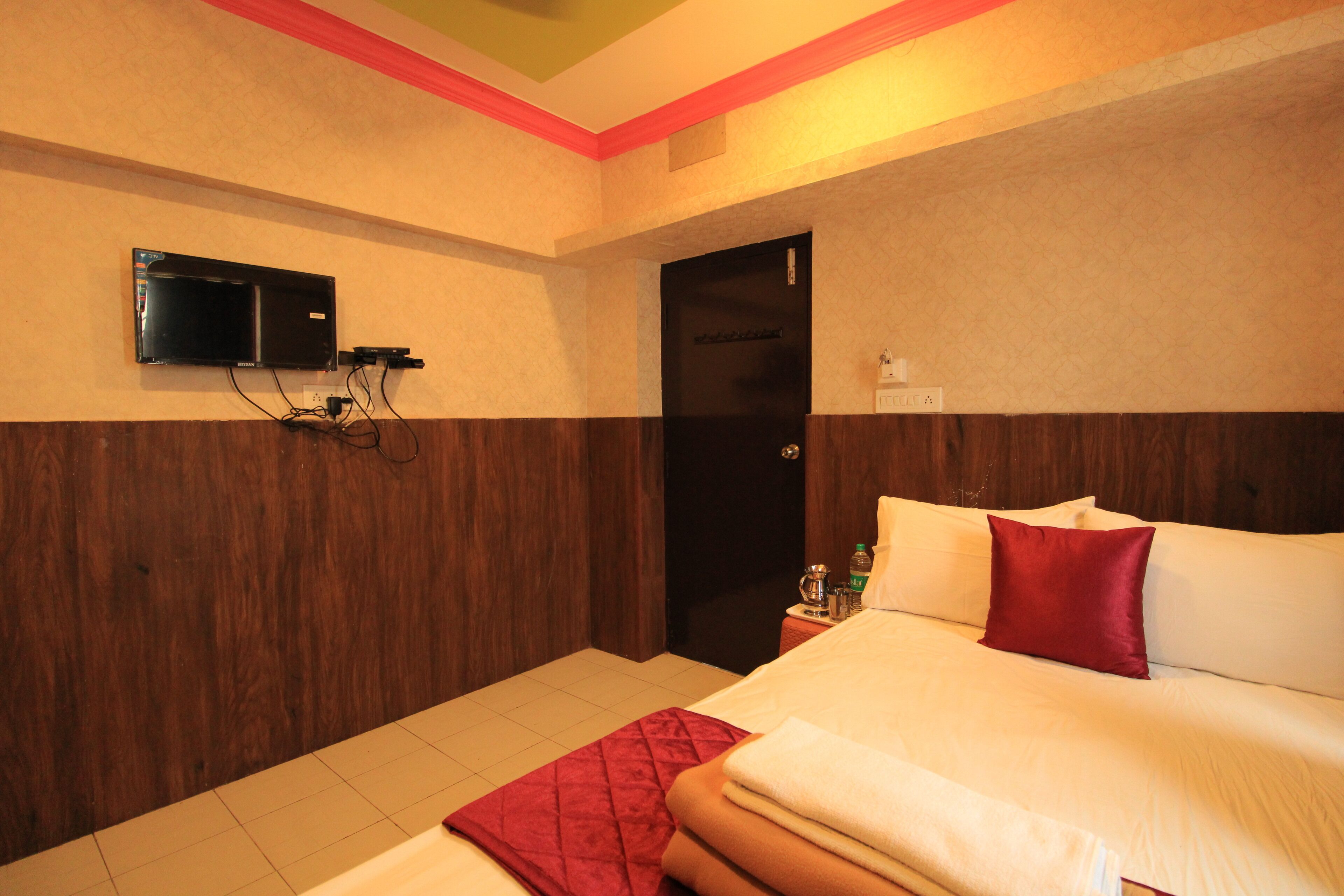 A hotel room with a bed, a TV mounted on the wall, and a door.