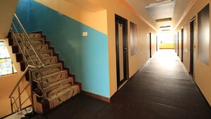 A long, narrow hallway with a staircase on the left, leading to an upper floor. The walls are painted in two colors, blue and beige. - M.G.R. Park Inn (Viluppuram)