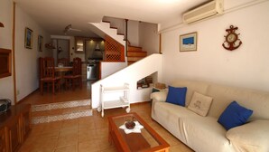 Una sala de estar con una escalera, un sofá, una mesa de centro y una zona de comedor con sillas y una mesa.