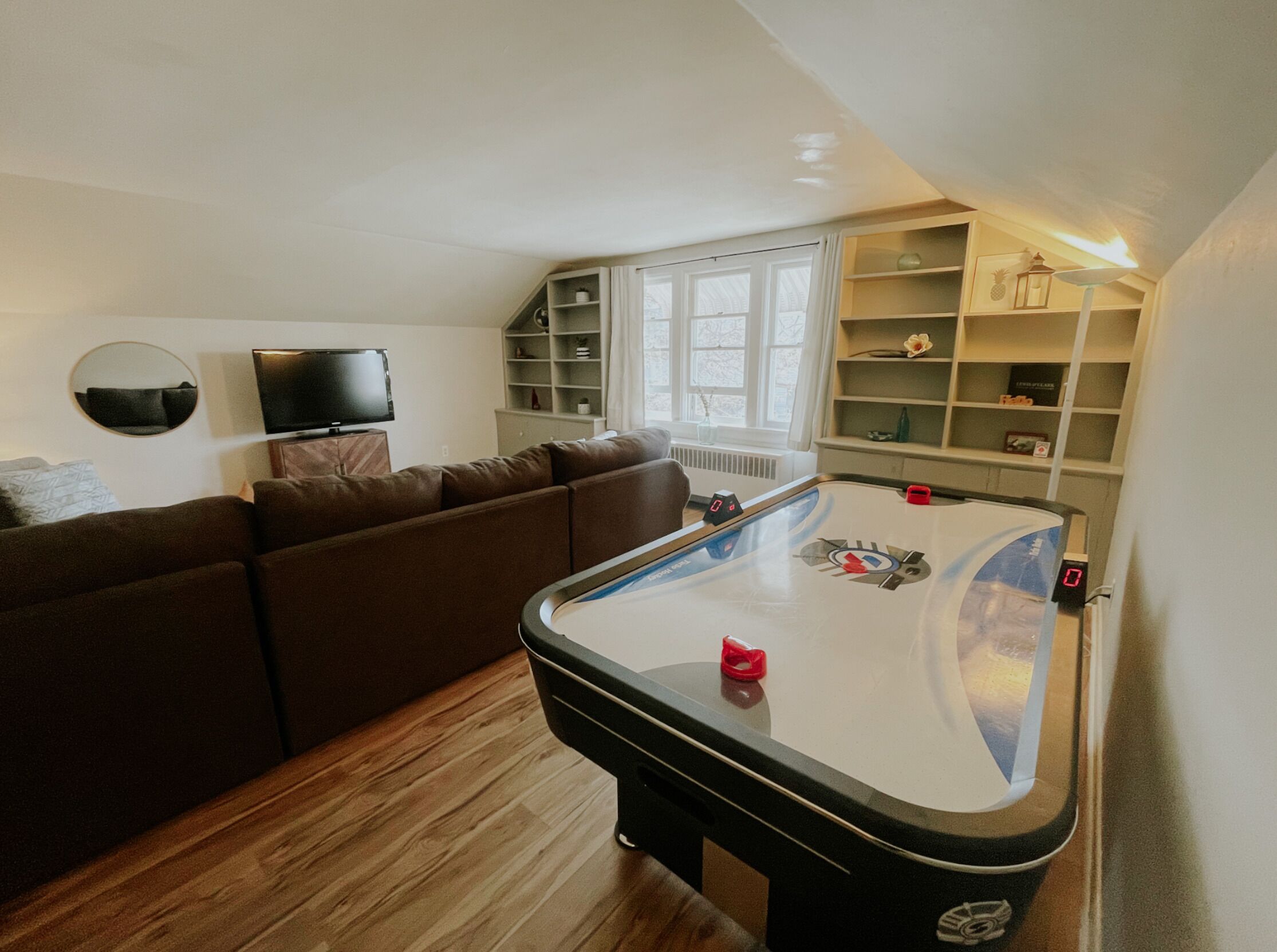 Un salon comprenant une table de billard, un canapé marron, un téléviseur et des étagères remplies de divers objets.