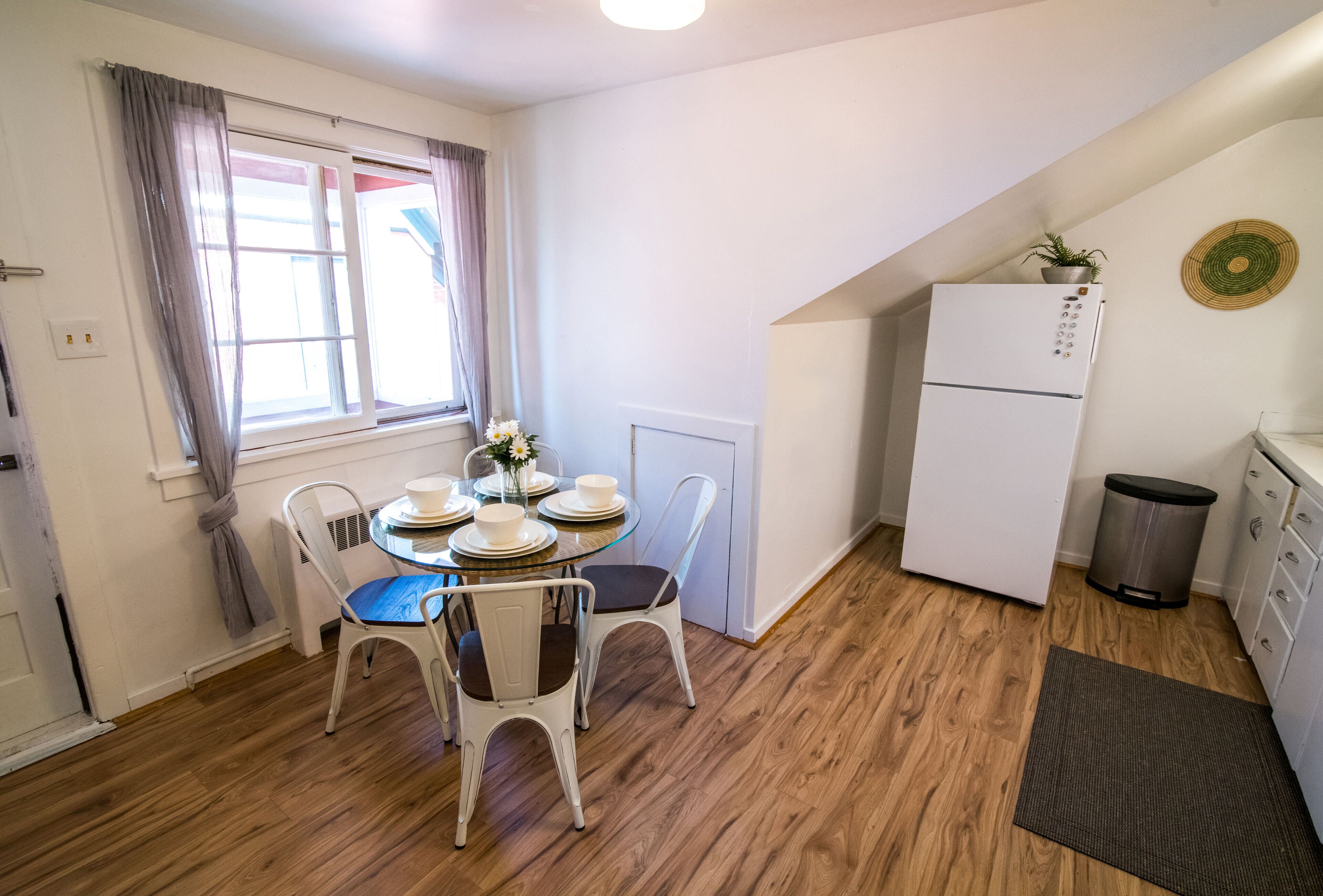 A compact kitchen with a refrigerator, a dining table with chairs, and a window with curtains.