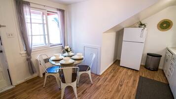 A compact kitchen with a refrigerator, a dining table with chairs, and a window with curtains.