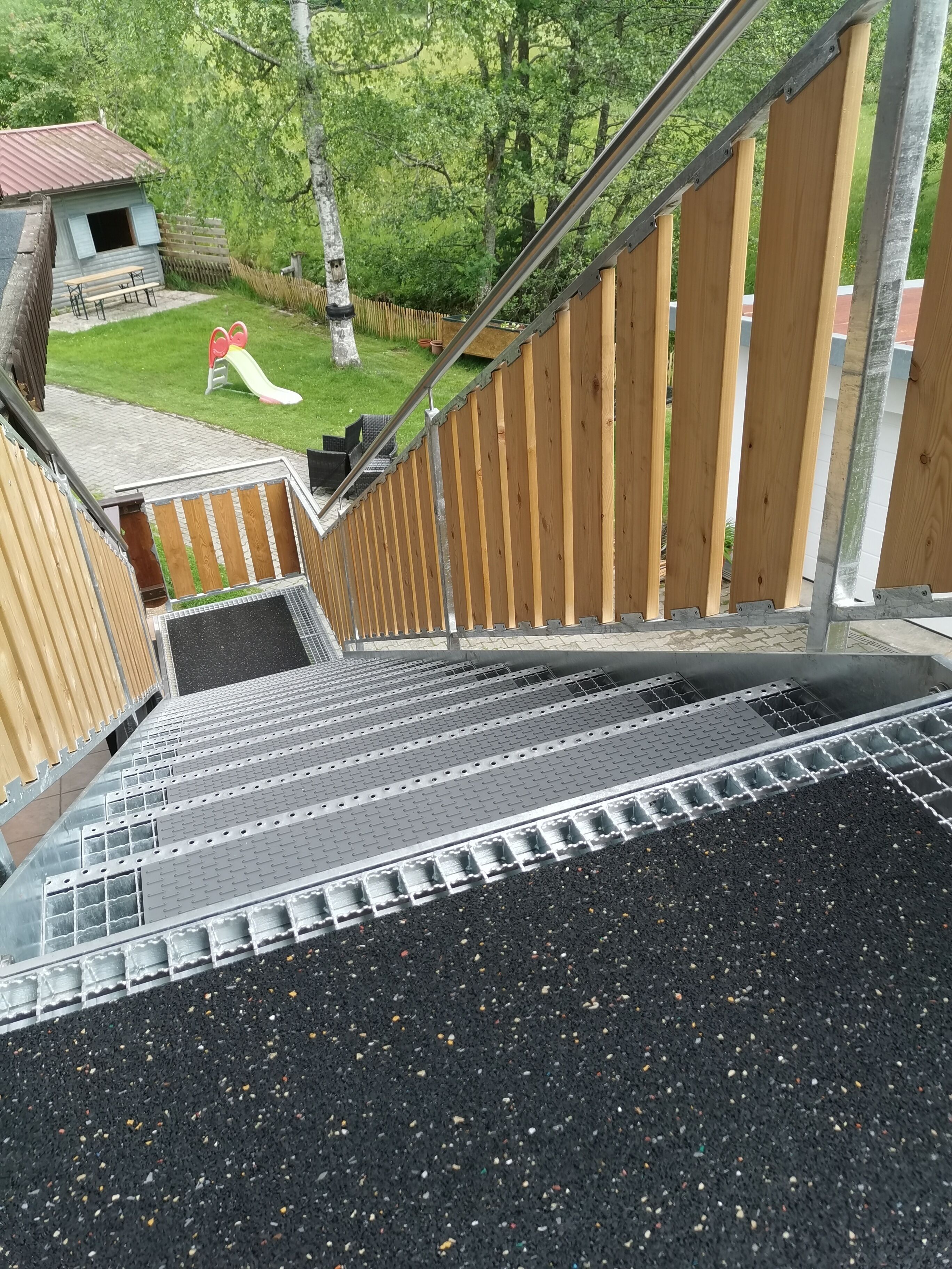Eine Treppe mit Metallgeländer, die zu einem Spielplatz mit Rutsche und einem kleinen Gebäude führt.