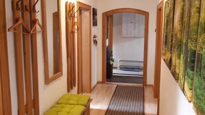 Un couloir doté d’un plancher en bois, d’un banc avec un coussin vert, d’étagères en bois fixées au mur, d’un miroir et d’un grand tableau accroché au mur de droite.