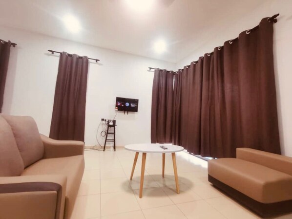 A living room with a beige sofa, a round coffee table, and a flat-screen TV mounted on the wall. - OYO Homes 90524 Dj Pegaso Serom Homestay (Sungai Mati)