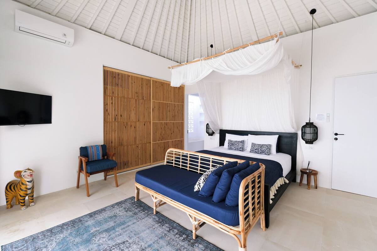 Un dormitorio con cama, televisor, silla, estatua de tigre y pantalla de bambú.