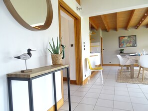 A modern interior with a wooden console table, a potted plant, a decorative bird sculpture, and a dining area with chairs and a table.