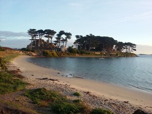 A beach with a sandy shore, a small boat, and a cluster of trees on a rocky outcrop. - PROPERTY 100 M FROM THE BEACH (Santec)