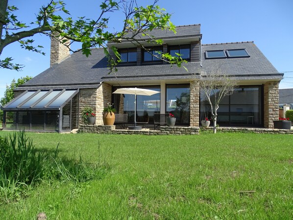 A two-story house with a stone facade, large windows, and a covered patio area.
