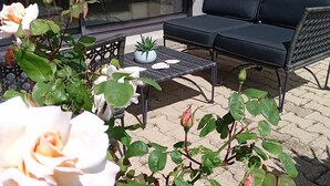 Uma área de pátio com assentos externos, uma planta em vaso e rosas floridas.