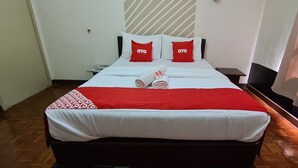 Une chambre d’hôtel avec un lit, deux oreillers rouges ornés du texte « OYO », une couverture rouge et blanche, et un plancher en bois.