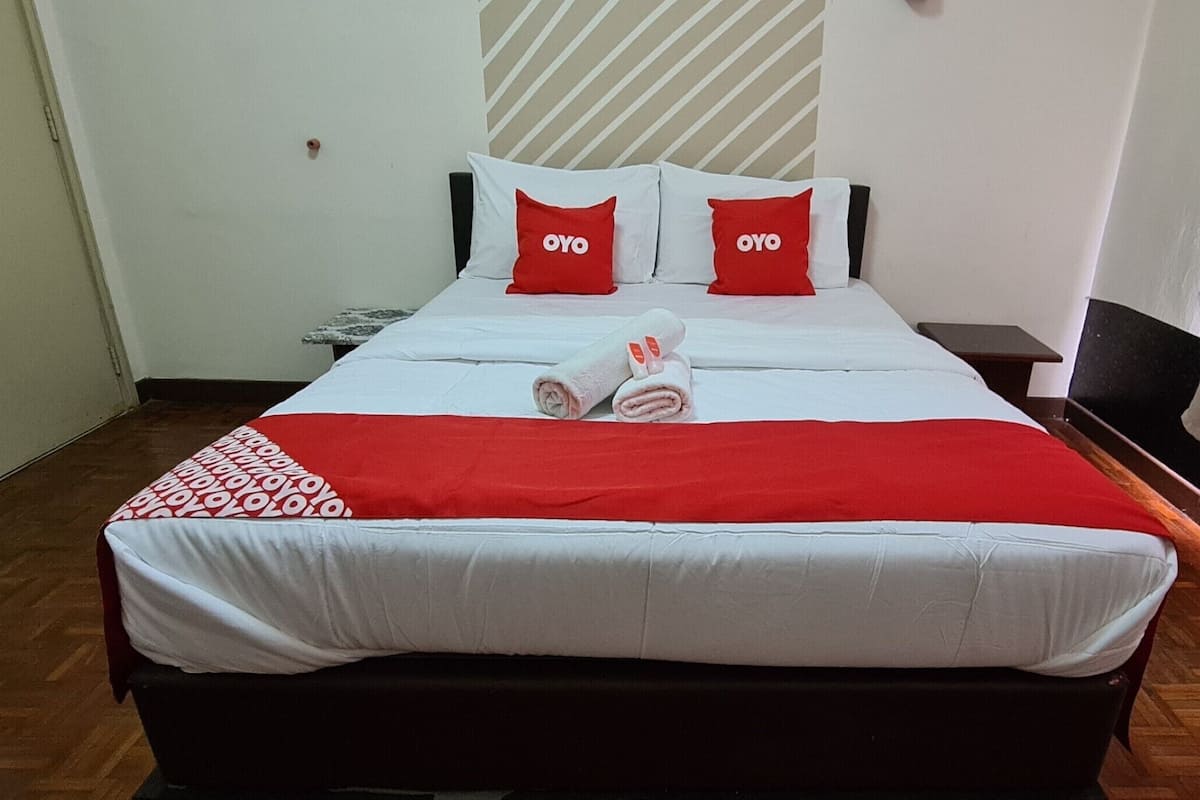 Een hotelkamer met een bed, twee rode kussens met de tekst 'OYO', een rood-wit dekbed en een houten vloer.