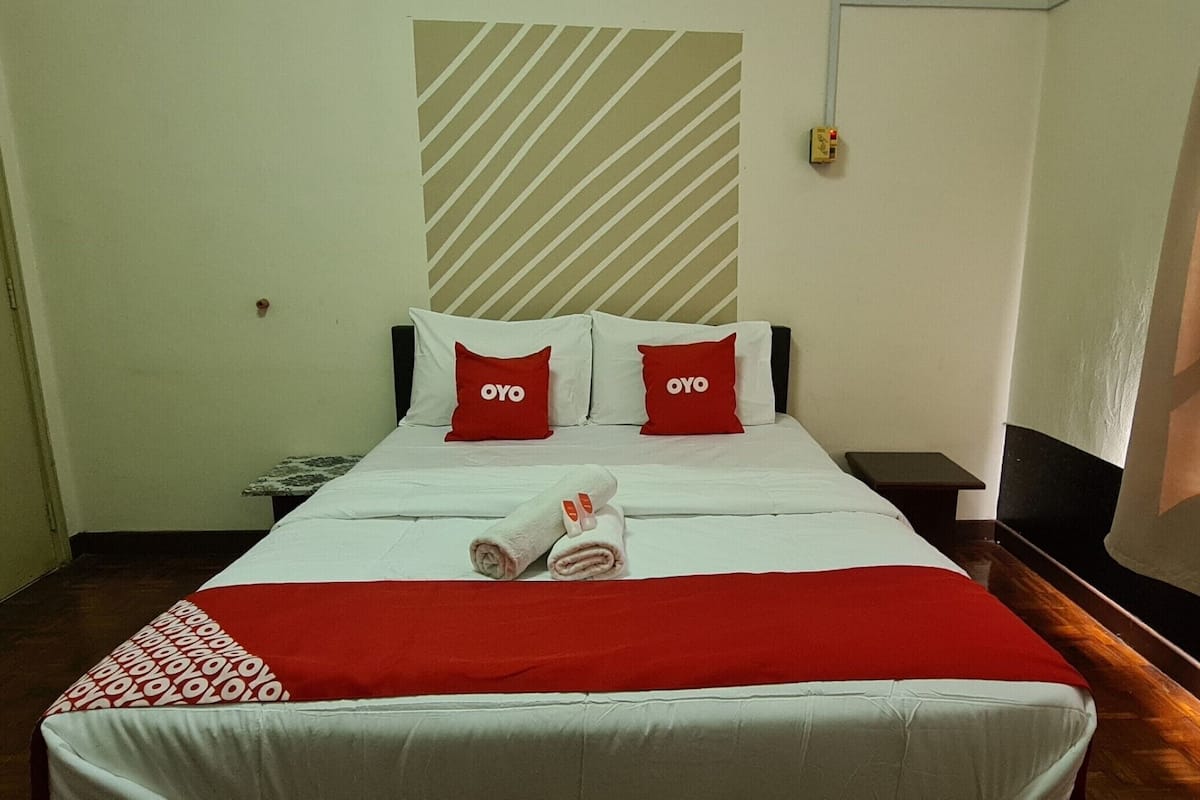 Een hotelkamer met een bed, twee rode kussens met 'OYO'-logo en een rood-witte plaid, plus een gestreept muurontwerp.
