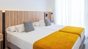 A hotel room with two beds, white bedding, and a wooden headboard.
