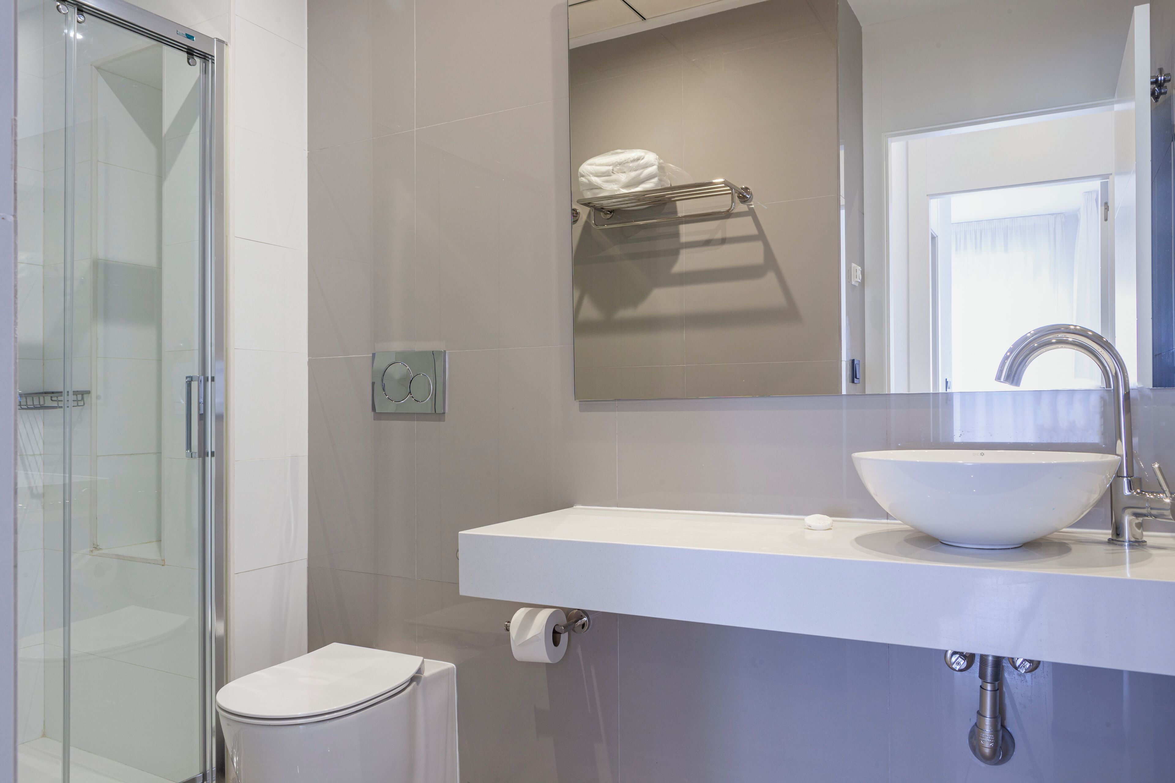 A modern bathroom with a glass shower enclosure, a white sink with a vessel basin, and a towel rack above the mirror.