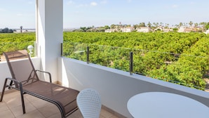 A balcony with a view of a vineyard, a white chair, a metal chair, and a small table.