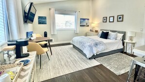 Moderni hotellihuone, jossa on sänky, työpöytä, tuoli ja suuri ikkuna.