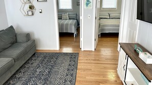 A modern living room with a grey sofa, a patterned rug, a wooden floor, and a TV on a wooden stand.