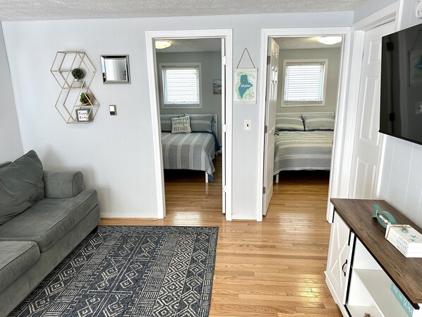 A modern living room with a grey sofa, a patterned rug, a wooden floor, and a TV on a wooden stand. - 2 BR condo. 1 min walk to the beach #105 (Old Orchard Beach)
