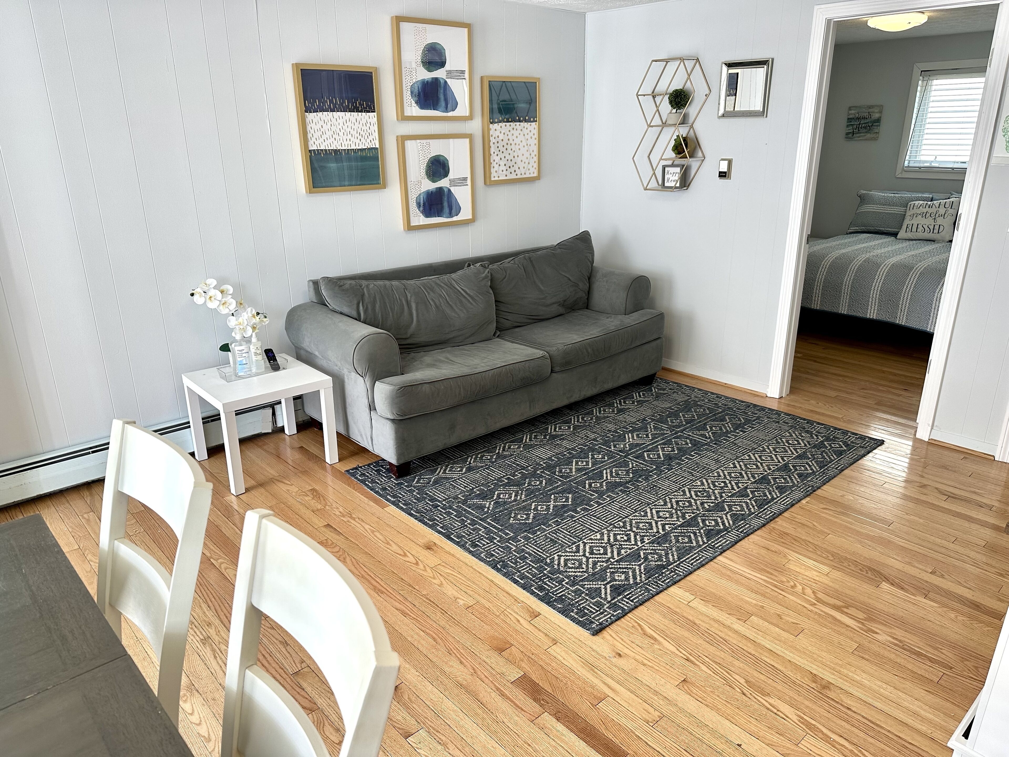 A modern living room with a grey sofa, a small white table, and a patterned rug.