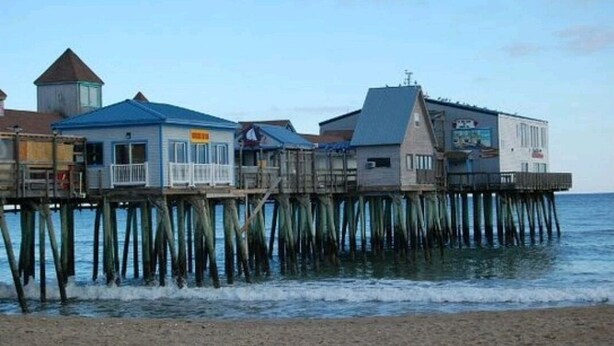 A waterfront property with multiple buildings on stilts over the water, including a blue building with a balcony and a white building with a sign.