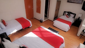 Habitación de hotel con dos camas, cada una con cubrecama rojo y blanco, suelo de madera, armario de madera y una mesita con lámpara.