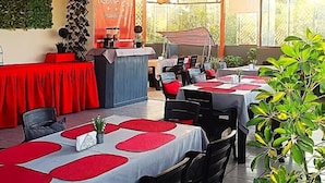 Un comedor interior con mesas cubiertas con manteles rojos y blancos, sillas negras y una barra con un banderín rojo.