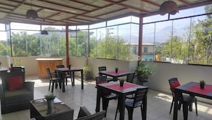 Un patio exterior con mesas y sillas, plantas en macetas y vistas a zonas verdes y montañas.