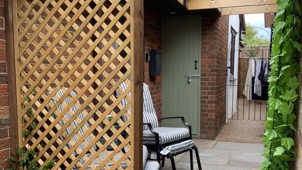 A wooden pergola with hanging light bulbs, a green door, and a seating area with striped chairs. - St. Mark's Court Holiday Homes - No1 (Marske-by-the-Sea)
