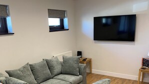 A modern living room with a grey sectional sofa, a flat-screen TV mounted on the wall, and a wooden floor. - St. Mark's Court Holiday Homes - No1 (Marske-by-the-Sea)