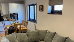 A modern living room with a grey sectional sofa, wooden dining table, and a kitchen in the background. - St. Mark's Court Holiday Homes - No1 (Marske-by-the-Sea)