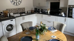 A modern kitchen with white cabinets, a built-in oven, and a large wall clock. - St. Mark's Court Holiday Homes - No1 (Marske-by-the-Sea)