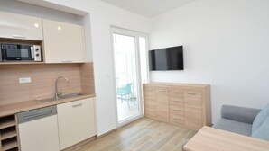 A compact kitchen with a microwave, sink, and wooden cabinets. There's a flat-screen TV mounted on the wall and a sofa in the living area. - Apartment Anna by Interhome (Murter/Jezera)