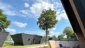 Una terraza moderna al aire libre con piso de madera, sillas de metal y un árbol grande.