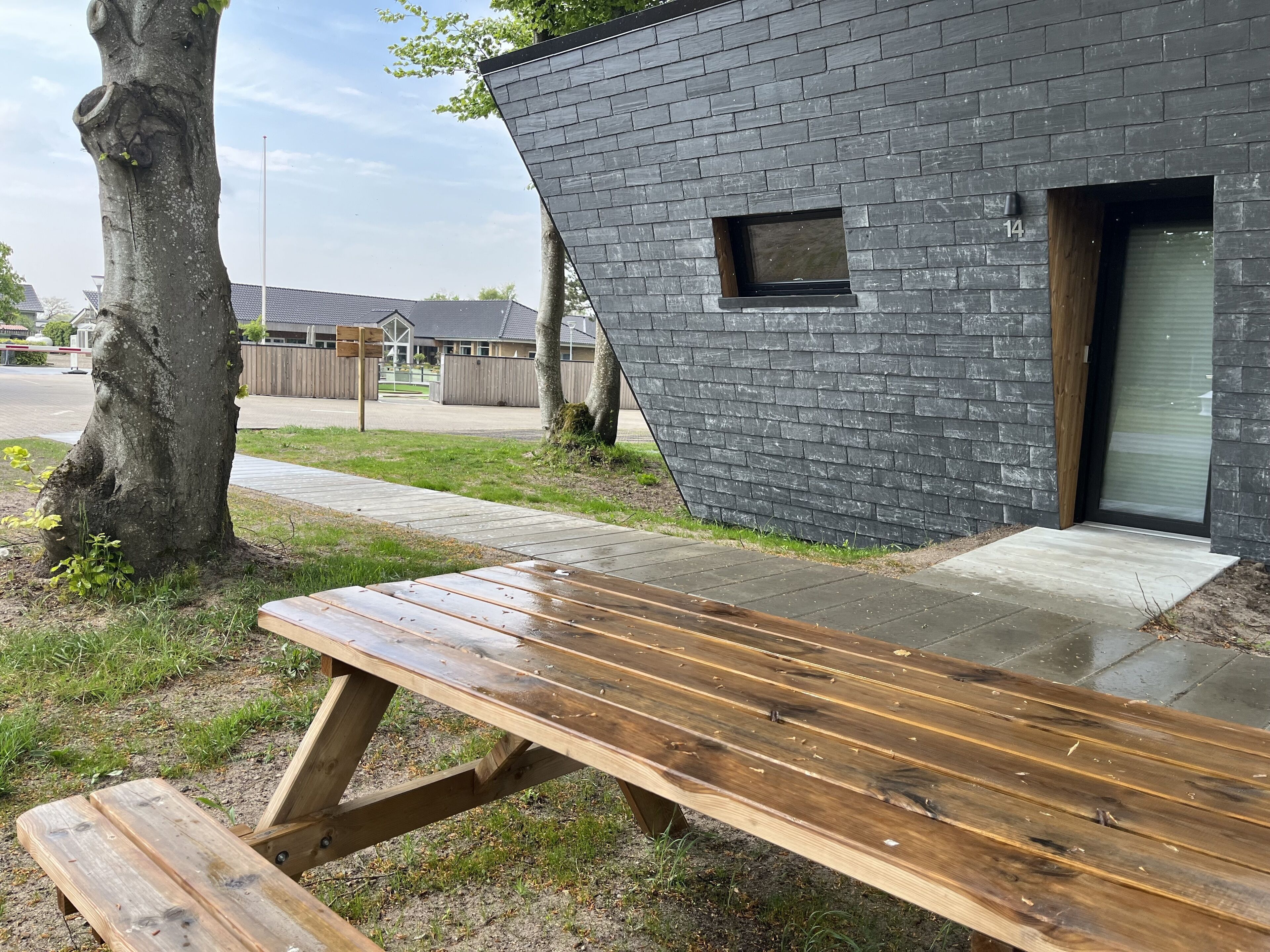 Un banco de madera frente a un edificio moderno con fachada de ladrillo y una ventana pequeña.