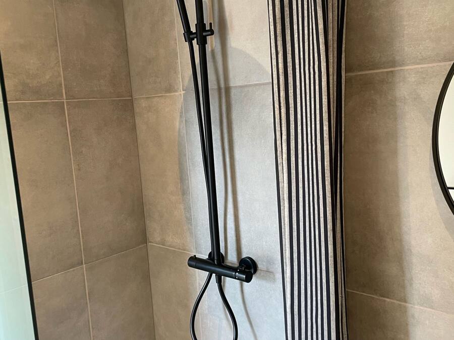 Doccia con soffione a mano e erogatore a pioggia, fissata a una parete con tenda a righe.