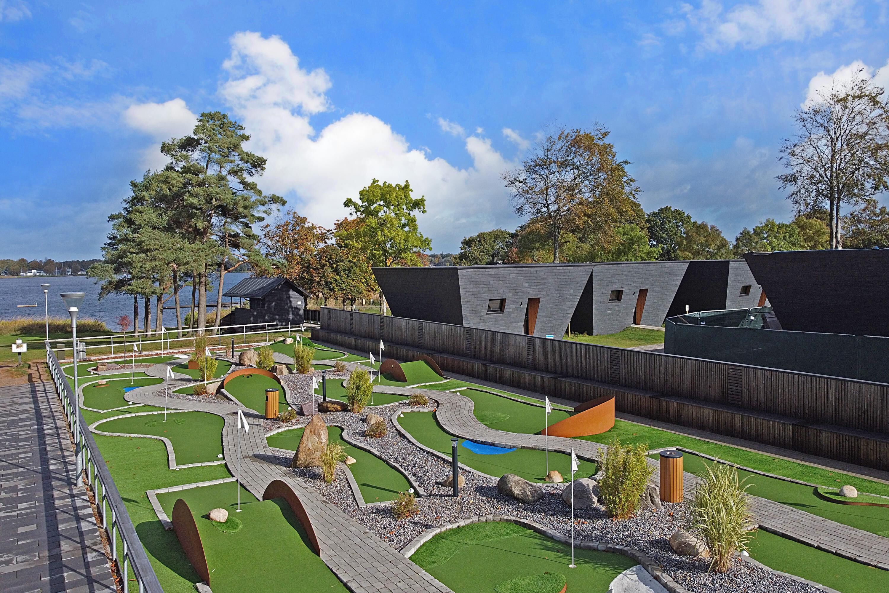 A landscaped area with pathways, artificial grass, and a body of water in the background.