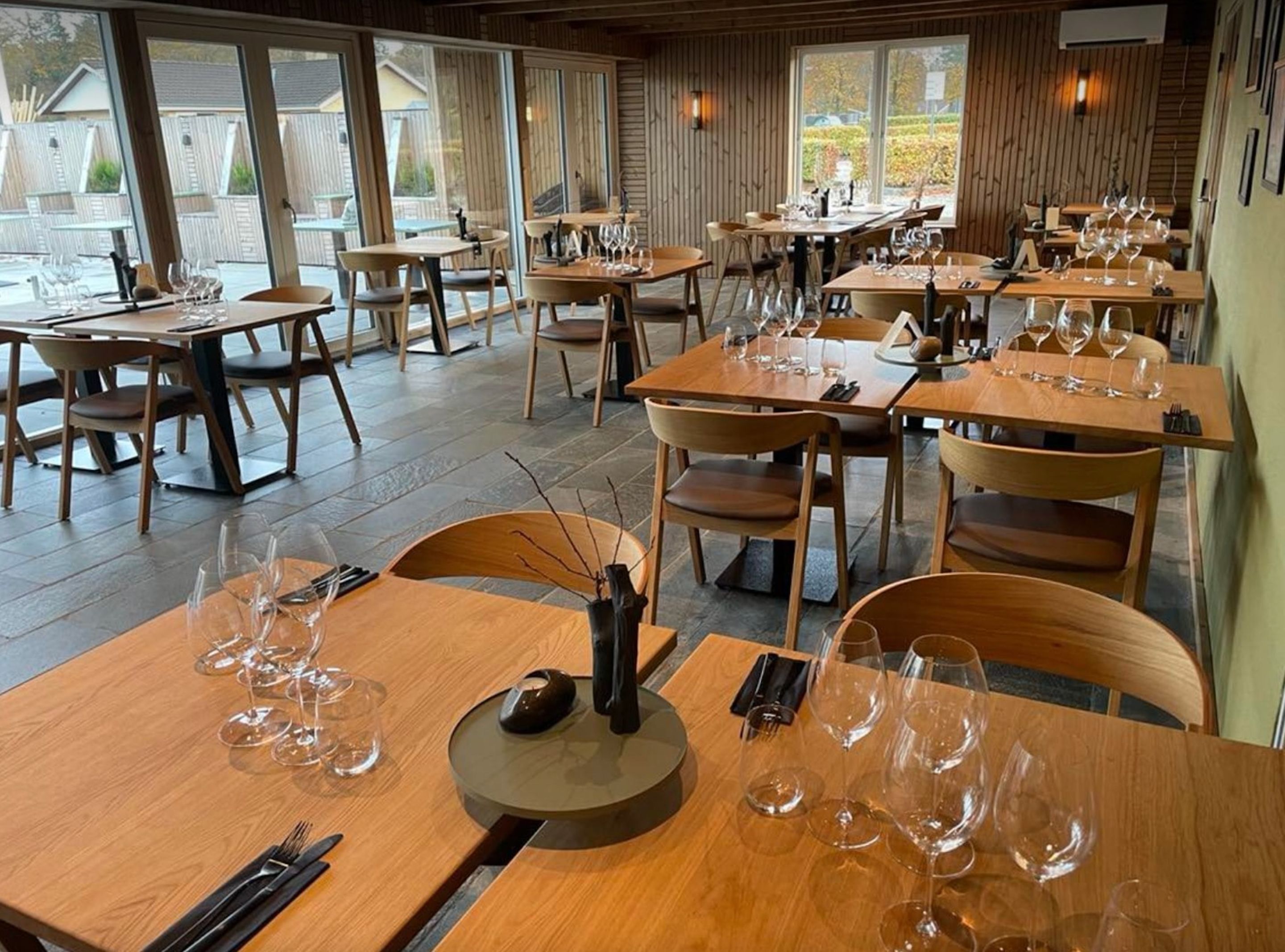 A restaurant with wooden tables and chairs, large windows, and a view of the outside.