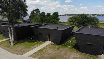 A row of modern, dark-colored cabins with flat roofs, situated on a grassy area with a paved walkway.