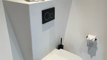 A modern bathroom with a white toilet, a black trash bin, and a towel rack with towels.