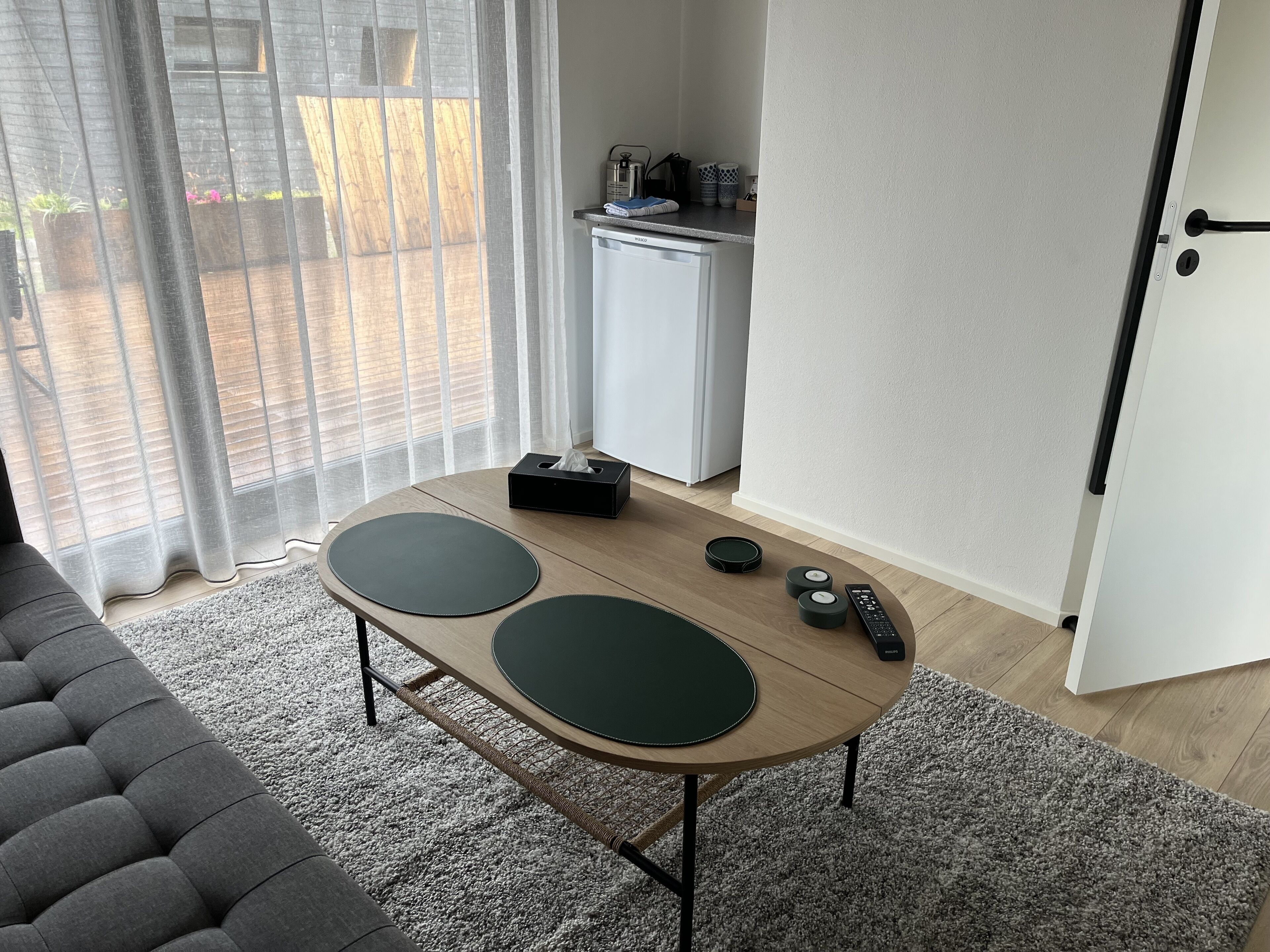 A modern living room with a round table, a sofa, and a kitchen area in the background.