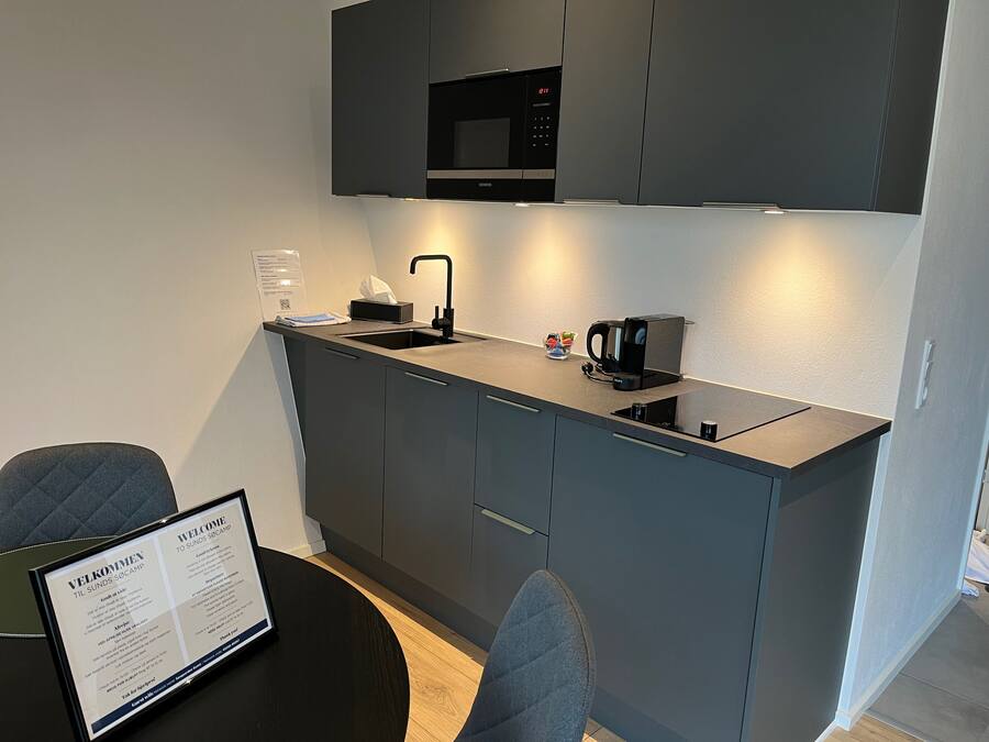 A modern kitchen with a built-in microwave, a coffee maker, and a sink. There is a framed welcome sign on the table.