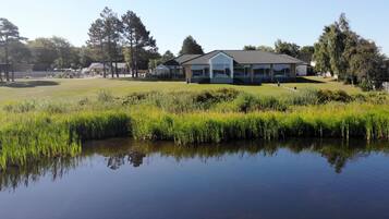 A building with a modern design, surrounded by a well-maintained lawn and a body of water reflecting the structure.